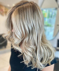 Blonde hair styled in loose curls with natural highlights, set against a bright salon interior.