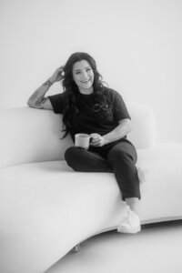 A woman sits relaxed on a sofa, holding a coffee mug. Portrait Photography by Karin Busch