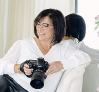 A woman sitting on a wood stool looking at the camera.