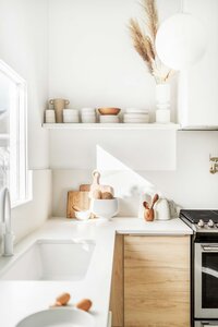 kitchen with white walls, white floating shelf with dishes, cutting boards and bowls with utensils