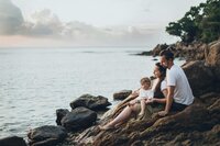 Eine Familie sitzt auf Felsen am Strand.