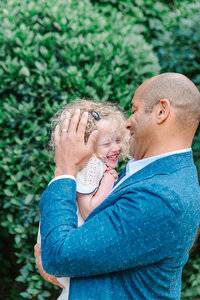 Father and daughter laughing together at Place des Vosges in the Marais, with the father gently stroking his daughter’s hair during a Paris family photoshoot.