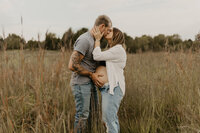 man and pregnant woman kissing in field
