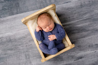 newborn boy in blue outfit in a cradle