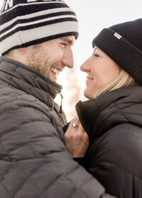 A happy couple snuggles in winter coats and beanies with big smiles