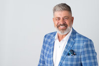 a smiling male in a plaid jacket against a white backdrop.  Captured in studio by Ottawa Headshot Photographer JEMMAN Photography COMMERCIAL