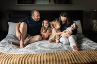 family with newborn and siblings sitting on bed