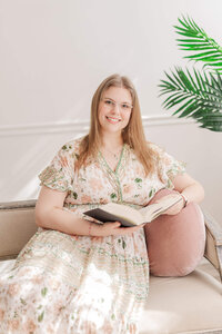 A woman sitting on a couch and holding a book in her hands.