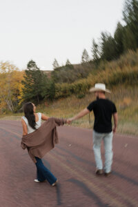 man and woman holding hands while walking down a asphalt road