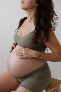 une photographie de studio sensigraphie qui représente une femme enceinte qui touche son ventre pendant une séance photo grossesse à la tour du pin