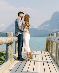 This beautiful engagement photograph captures the couple standing on a wooden bridge by Bow Lake in Banff National Park. The stunning lake and surrounding mountains provide a breathtaking backdrop, making for a romantic and memorable moment.