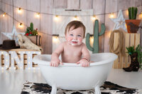 Smiling boy in a mini white tub, holds on to the ledge of the tub surrounded by western props.
