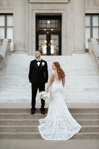 bride and groom on wedding day in front of church with wedding gown and bouquet
