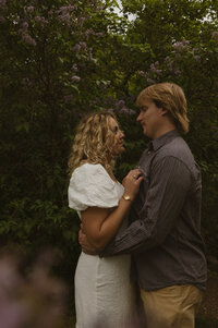 A husband holds his pregnant wife's belly while she holds his chin.