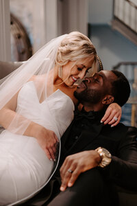 A newlywed sitting on their partners lap as they are about to kiss