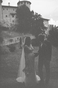 bride and groom standing in front of castle in b&w