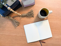 Top-down view of journaling setup with open notebook, coffee mug, beads, and motivational calendar
