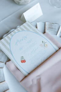 Watercolor wedding menu tucked in a napkin at a placesetting featuring full service design by Life in Letters representing full service design and calligraphy by Life in Letters.