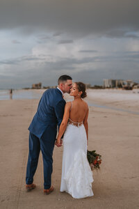 bride and groom kissing and holding hands on the beach