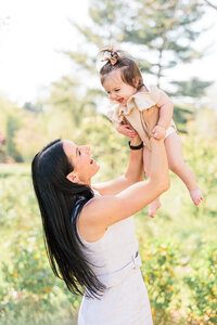 A joyful moment of a mother holding up her smiling baby outdoors.