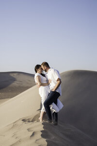 A newly engaged couple share a big kiss on a sand dune at the Amargosa Big Dune Recreation Area