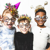 Three children wearing party hats and glasses for New Year's Eve