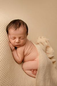 newborn baby boy holding a felt heart on a blue blanket
