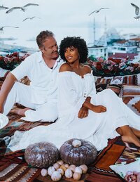 Beautiful couple sit on beautiful rugs and enjoy tea overlooking the city