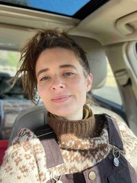 A woman in a car, dressed in a sweater and overalls, reviewing Brave Nature School for Unica Formo.
