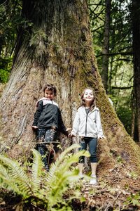 a brother and sister pose next to the trunk of a big tree