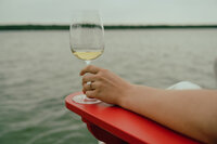 Engaged woman holds a glass of white wine set against the Ottawa River while showing off her engagement ring