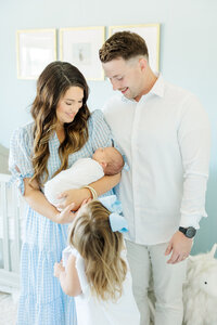 postpartum mom wearing blue and white dress kissing newborn baby girl in pottery barn nursery