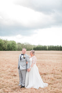 Bride in a cap sleeve gown and a groom in a navy three piece suit and floral tie, sitting in a greenhouse. Luxoumont Farm PA