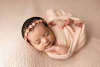 Baby girl wrapped in light peach colored blanket with bow headband.