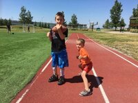 Two children in a track field, one of whom is Joshua, a patient of Lethbridge Orthotics, now able to run and play without falling.