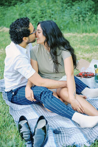 A couple sit on a picnic blanket happily embraced after a successful Proposal in New York City, Queens. Photo taken by Corey Lamar Photography