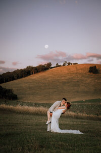 Groom dipping bride and kissing with rolling hills and moon in the background