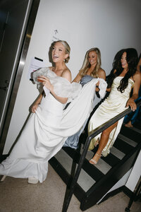 Bride walking down stairs laughing with bridesmaids before ceremony, captured in documentary-style luxury wedding photography.