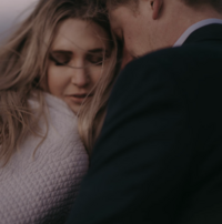 A bride and groom snuggle close. The brides eyes are closed facing the camera, the groom's head is nuzzled against the bride