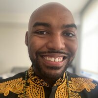 a young, bold, Black man, client of Workhap, is looking and smiling at the camera