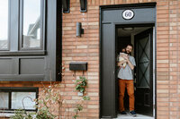 A person stands in a doorway holding a dog, captured in the style of family photography Toronto loves. The building features a brick exterior with a black-framed door, above which the round number "60" is displayed.