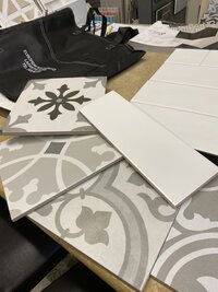 A collection of patterned tile samples, white subway tiles, and design materials laid out for a home remodeling selection process.