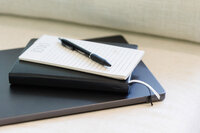 A notebook stacked on top of a book, stacked on top of a Macbook