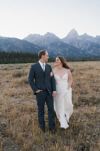 Bride and groom running through the Grand Tetons National Park and looking at each other her laughing. 