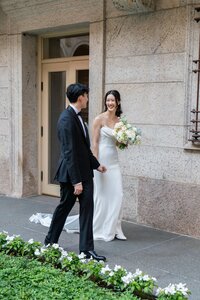 Rhode Island Wedding Photographer | Kelsey Sheehan Photography Timeless Rhode Island Weddings | A bride and groom walk outside, the bride in a white gown holding a bouquet. Both are smiling, creating a joyful and romantic atmosphere.