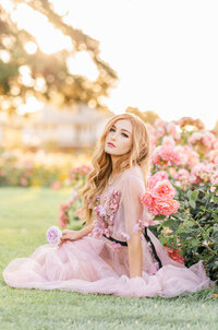 A modeled shoot by Bay area photographer, a woman in a light and airy gown sits in a rose garden.