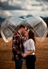 A couple huddles under clear umbrellas in a field in the adirondacks
