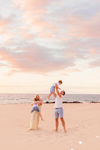 family of four plays on the beach together during their family photo session in Hawaii