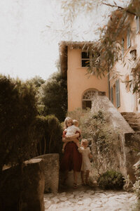 photo maman porte bebe dans les bras et tient la main de sa fille dans le jardin serre de la madone menton