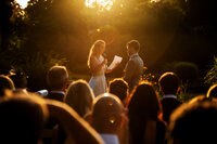 Bruidspaar spreekt hun geloften uit bij Groot Warnsborn tijdens zonsondergang, met een warme lensflare die de ceremonie intiem en sfeervol maakt – vastgelegd door Juliette Fotografie.